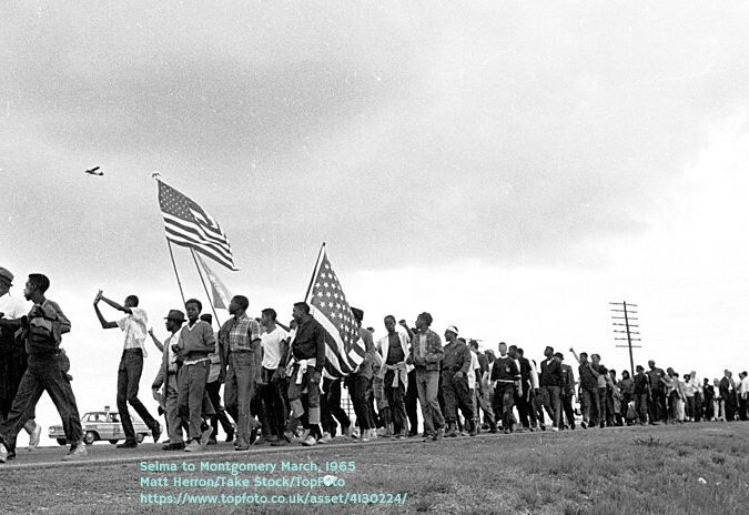 Selma to Montgomery March for voting rights: 1965 -  Marchers and flags cross the horizon. Airplane is reconnisance plane of Alabama National Guard on lookout for threats to march.  Selma-Montgomery, Alabama  3/21/1965